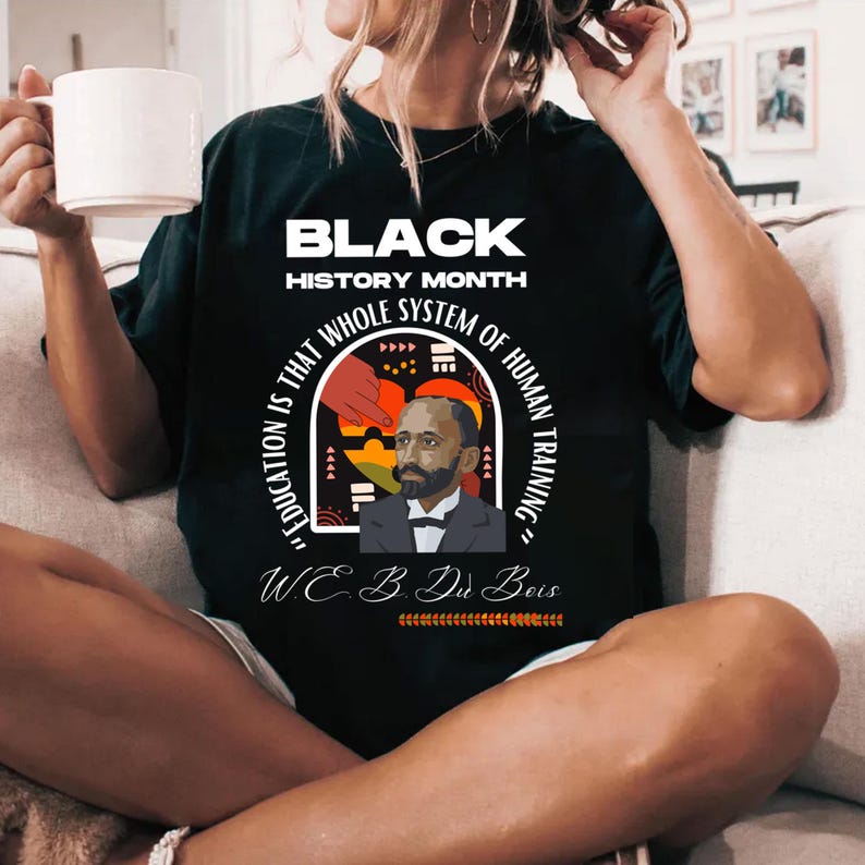 May include: Black t-shirt with a graphic design featuring a portrait of W.E.B. Du Bois and the quote "Education is that whole system of human training." The text "Black History Month" is at the top of the design.
