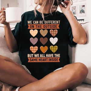 May include: Black t-shirt with a message that reads "We can be different on the outside, but we all have the same heart inside". The message is surrounded by a row of colorful hearts with different patterns.