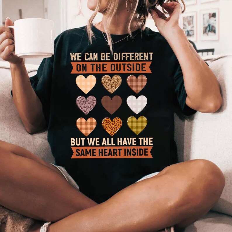 May include: Black t-shirt with a message that reads "We can be different on the outside, but we all have the same heart inside". The message is surrounded by a row of colorful hearts with different patterns.