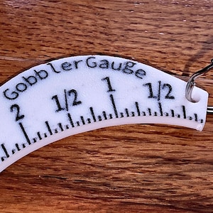 May include: White plastic turkey gobbler gauge with a keychain ring. The gauge measures from 1/2 inch to 2 inches.