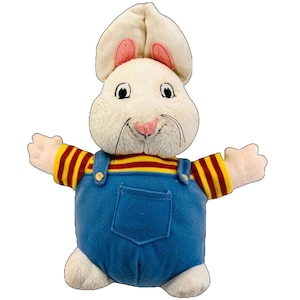 May include: A plush white rabbit toy with large ears and a pink nose. The rabbit wears a blue denim overall with a yellow and red striped shirt. The toy has outstretched arms and a smiling expression.