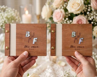 May include: Two rectangular wooden vow books with gold-tone metal binding screws. Each cover features mother-of-pearl inlay letters B and F, a delicate leaf illustration, and the printed text Her vows 09.16.26 on a light-colored fabric spine.
