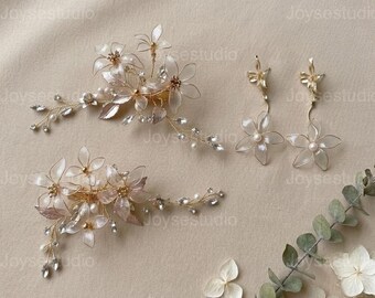 May include: Elegant bridal hair accessories and earrings. The set includes two floral hair clips and a pair of dangle earrings. The hair clips and earrings feature delicate, translucent flowers, crystals, and pearls, all set on gold-toned wire.