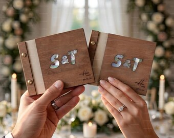 May include: Two square wooden vow books with a light-colored fabric spine secured by two gold-tone metal screws. The front covers feature the inlaid mother-of-pearl letters S & T, with the text Vows and the date 09.16.24 engraved below.