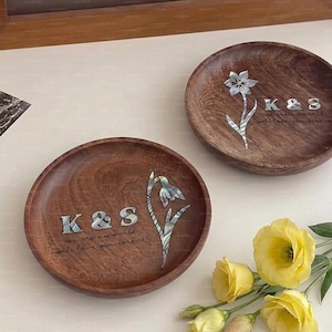 Könnte beinhalten: Zwei runde Holztabletts mit floralen und textlichen Details. Jedes Tablett zeigt die Initialen "K&S" und die Inschrift "You are my world, I will love you forever." Die floralen Designs sind mit einem perlmuttartigen Material eingelegt. Gelbe Blumen sind im Vordergrund.