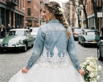 May include: A light blue denim jacket with white lace detailing and the text "Mrs. William" on the back. The jacket is worn over a white tulle skirt. A bouquet of white flowers is held in the hand.