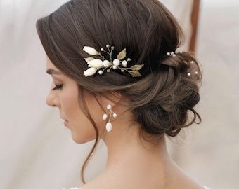 May include: A woman's hair styled in an updo, adorned with a gold and pearl hairpiece. The hairpiece features white fabric flowers, gold leaves, and small pearls. The woman is also wearing pearl earrings. The overall theme is bridal or formal occasion.