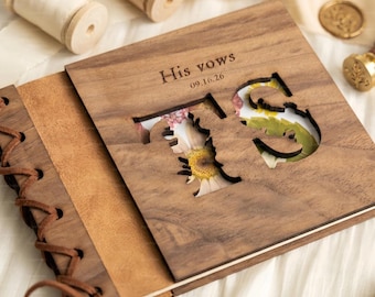 May include: A square wooden album with a dark brown finish, featuring a cutout of the letters T and S. The cover is engraved with the text His vows 09.16.26. The spine is made of tan leather and is bound with brown leather lacing.