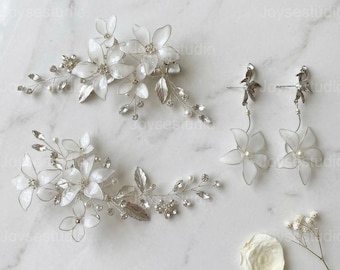 May include: A bridal jewelry set featuring two floral hair combs and a pair of earrings. The hair combs and earrings are adorned with white flowers, silver leaves, and sparkling crystals. The earrings have a dangling flower design.