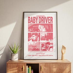 May include: A pink and white poster with the title "Baby Driver" in bold red letters. The poster features a collage of images from the movie, including a man in a car, a man walking down a street, and a couple kissing. The poster also includes the director's name, Edgar Wright, and the names of the actors:  Elioot James Spitzer, Jamie Foxx, and Jon Bernthal.