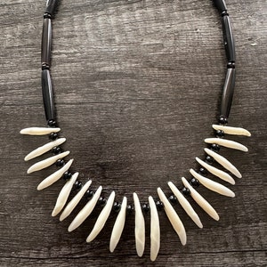 May include: A necklace made of black and white beads. The white beads are shaped like teeth and the black beads are round. The necklace is on a wooden surface.