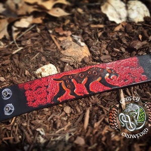 May include: A black leather bracelet with silver studs and a red background. The bracelet features a black silhouette of a panther with white spots.