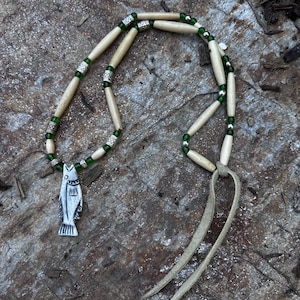 May include: A white bone and green glass bead necklace with a silver fish pendant and a brown leather cord.