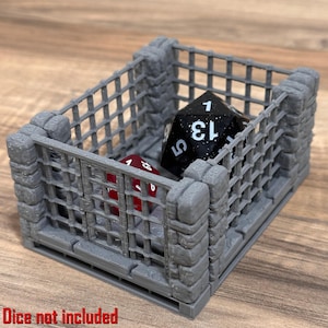 May include: A gray, 3D-printed dice jail with a rectangular cage design. Inside the cage are two dice: a black D20 and a red D6. The text "Dice not included" is at the bottom. The jail is designed to hold dice for tabletop games.