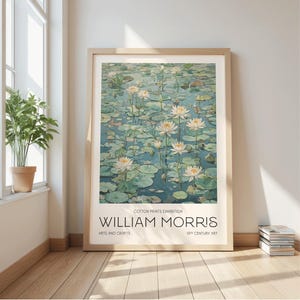 Può includere: Una stampa artistica incorniciata raffigurante una serena scena di stagno con ninfee bianche e foglie di ninfea. L'opera è intitolata "WILLIAM MORRIS" con il testo "COTTON PRINTS EXHIBITION" e "ARTS AND CRAFTS 19TH CENTURY ART". La cornice è in legno chiaro.