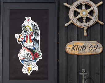 May include: A framed black and white print of a sailor's grave tattoo with a red rose and an anchor. The print is hanging on a black wooden wall with a wooden ship's wheel and a sign that reads "Klub 69".
