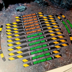 May include: A collection of straight and curved game markers featuring black and yellow hazard stripes. The markers are printed with the text DEPLOYMENT ZONE in either orange or green, accompanied by a small white diamond-shaped icon.