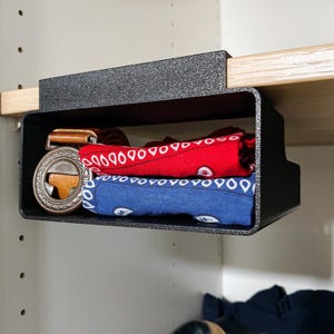 May include: A black plastic shelf organiser with a red and blue bandana and a brown leather belt with a silver buckle inside.