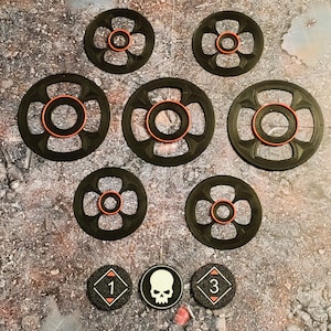 Könnte beinhalten: Eine Sammlung von schwarzen und orangefarbenen Spielsteinen. Sieben kreisförmige Komponenten mit einem zentralen Loch und einem orangefarbenen Ring sind zu sehen. Drei kleinere, kreisförmige Spielsteine zeigen einen Totenkopf, die Zahl 1 und die Zahl 3.