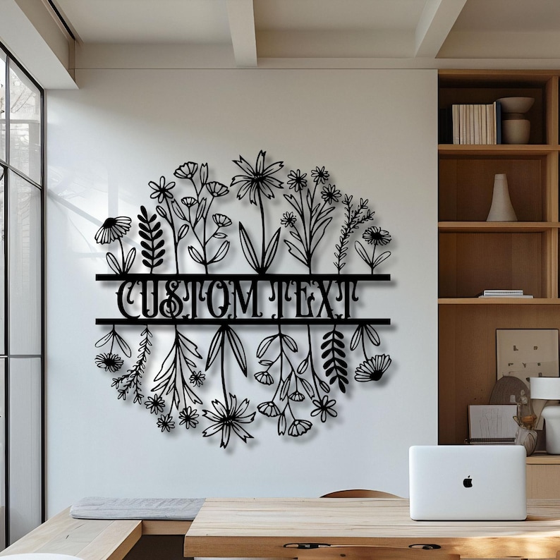 May include: Black metal floral wall art with the text "CUSTOM TEXT" in a cursive font. The art features a circular arrangement of various flowers and foliage, suitable for home decor.