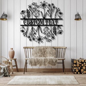 May include: Black metal floral wall art with the text "CUSTOM TEXT" in a circular design. The art piece is mounted on a white wooden wall above a wooden bench with a faux fur throw.