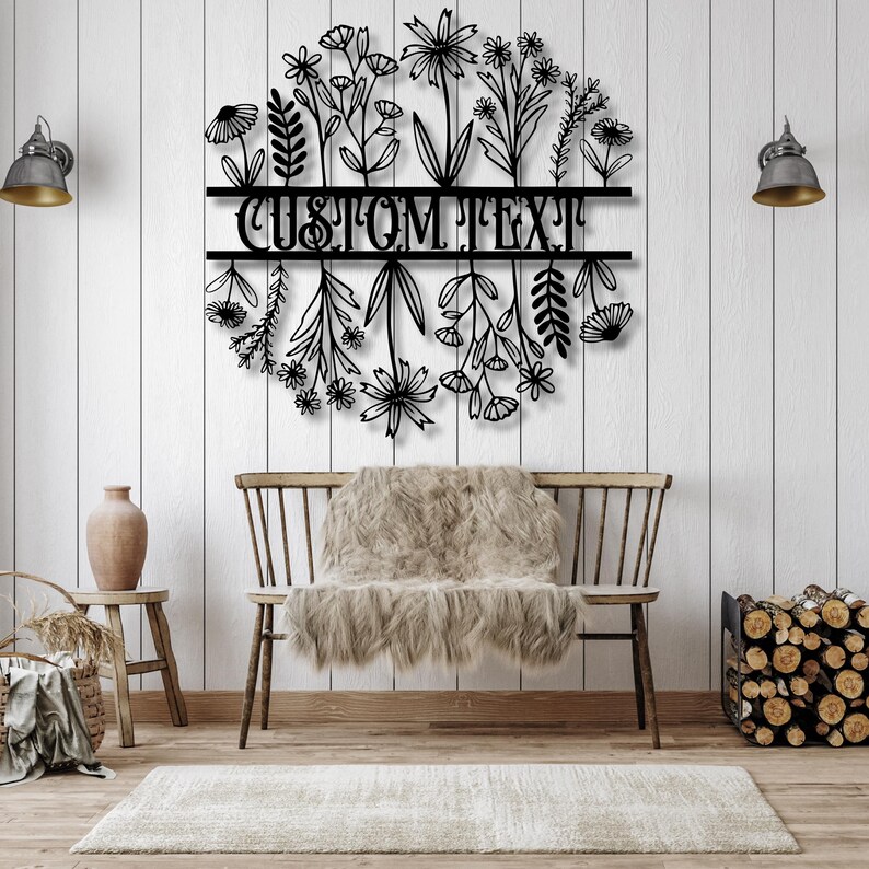 May include: Black metal floral wall art with the text "CUSTOM TEXT" in a circular design. The art piece is mounted on a white wooden wall above a wooden bench with a faux fur throw.