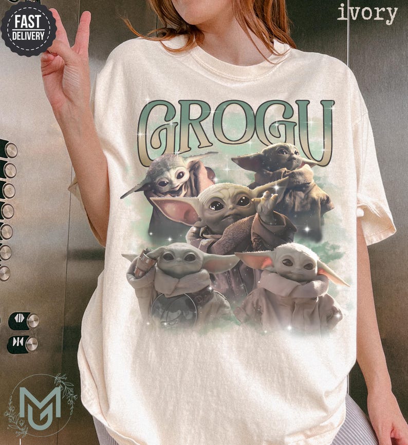 May include: An ivory short-sleeve t-shirt featuring a graphic print of five Grogu characters from The Mandalorian. The text GROGU is printed in a large, stylized green and white font above the characters, which are set against a soft green background.