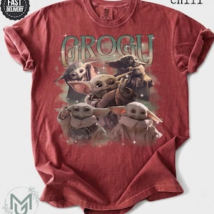 May include: A chili red short-sleeve t-shirt featuring a graphic print of four Grogu characters. The text GROGU is printed in a large, stylized font above the characters, accented with small white star-like sparkles throughout the design.