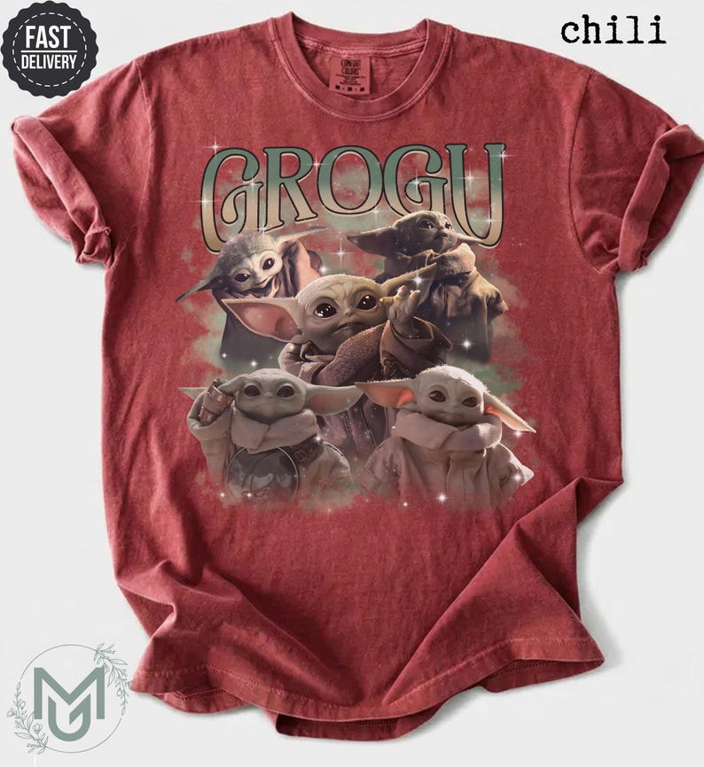 May include: A chili red short-sleeve t-shirt featuring a graphic print of four Grogu characters. The text GROGU is printed in a large, stylized font above the characters, accented with small white star-like sparkles throughout the design.