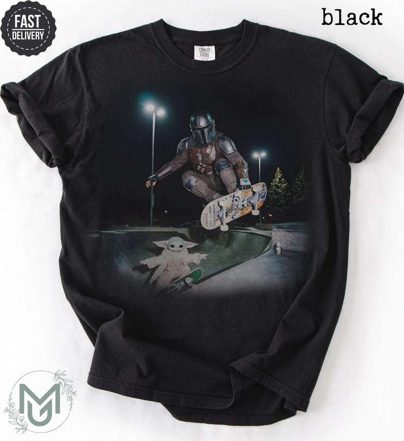 K&ouml;nnte beinhalten: Ein schwarzes T-Shirt mit einem Grafikdruck, der eine Figur in metallischer R&uuml;stung zeigt, die nachts in einem Skatepark einen Skateboard-Trick ausf&uuml;hrt, mit einem kleinen gr&uuml;nen Wesen auf einem Skateboard darunter. Der Text "black" steht oben rechts.