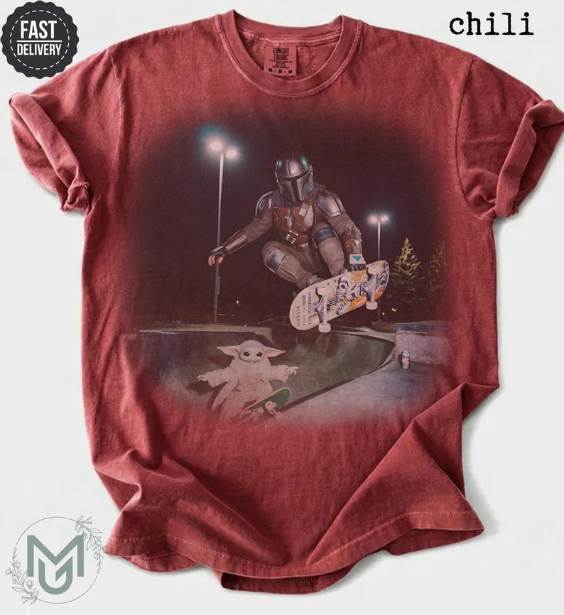K&ouml;nnte beinhalten: Ein chilirotes Kurzarm-T-Shirt mit einem Grafikdruck, der eine Figur in Metallr&uuml;stung zeigt, die nachts in einem Park skatet, mit einer kleinen gr&uuml;nen Kreatur auf einem Skateboard darunter. Das Shirt hat einen Rundhalsausschnitt und eine Vintage-Waschung.