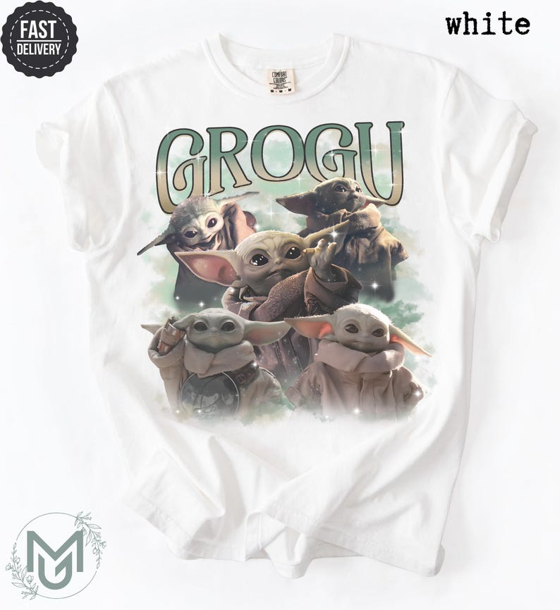 May include: A white short-sleeve t-shirt featuring a graphic print of four Grogu characters. The text GROGU is printed in a large, stylized green and white font above the characters. The design includes soft green cloud-like accents and sparkles.