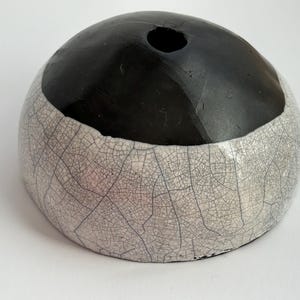 May include: A ceramic vase with a black top and a white bottom with a crackled glaze. The vase has a round shape and a small opening at the top.
