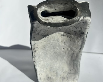 May include: A white ceramic vase with a black rim and a speckled glaze. The vase has a rectangular shape with a rounded top.