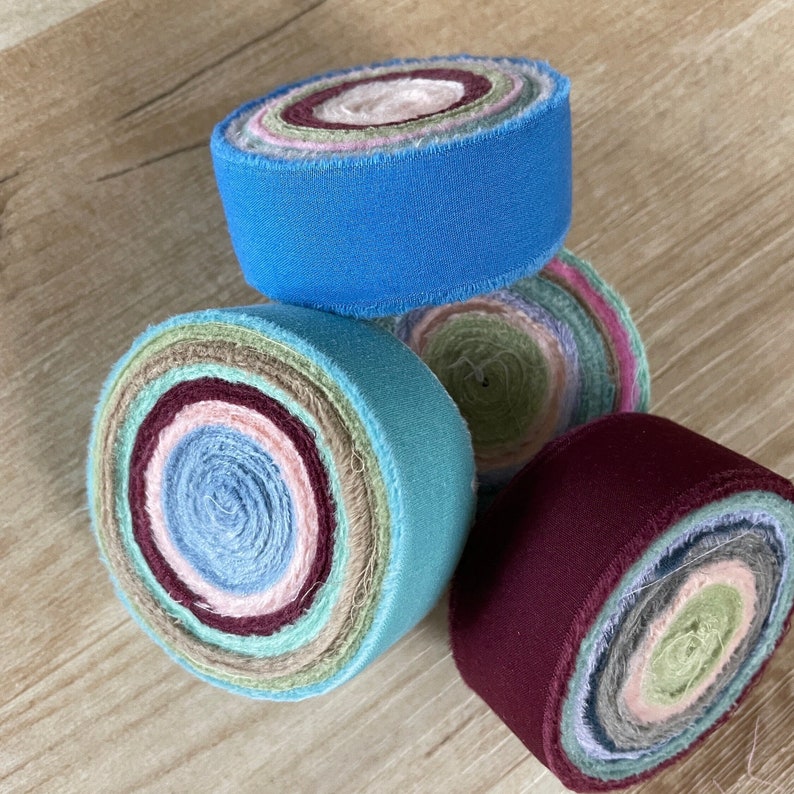 May include: Four rolls of fabric scraps in various colors, including blue, green, pink, and burgundy. The fabric is rolled into a circle and has a raw edge.