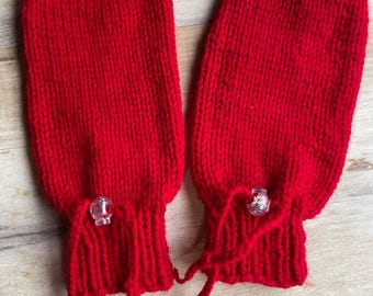 Könnte beinhalten: Ein Paar leuchtend rote Strickfäustlinge. Jeder Fäustling hat ein geripptes Bündchen und einen transparenten Kunststoffknebel mit roter Garnkordel. Die Fäustlinge sind aus dickem, warmem Garn gefertigt.