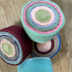 May include: Four rolls of fabric scraps in various colors, including teal, burgundy, pink, and green. The fabric is rolled into a circle and the layers are visible.