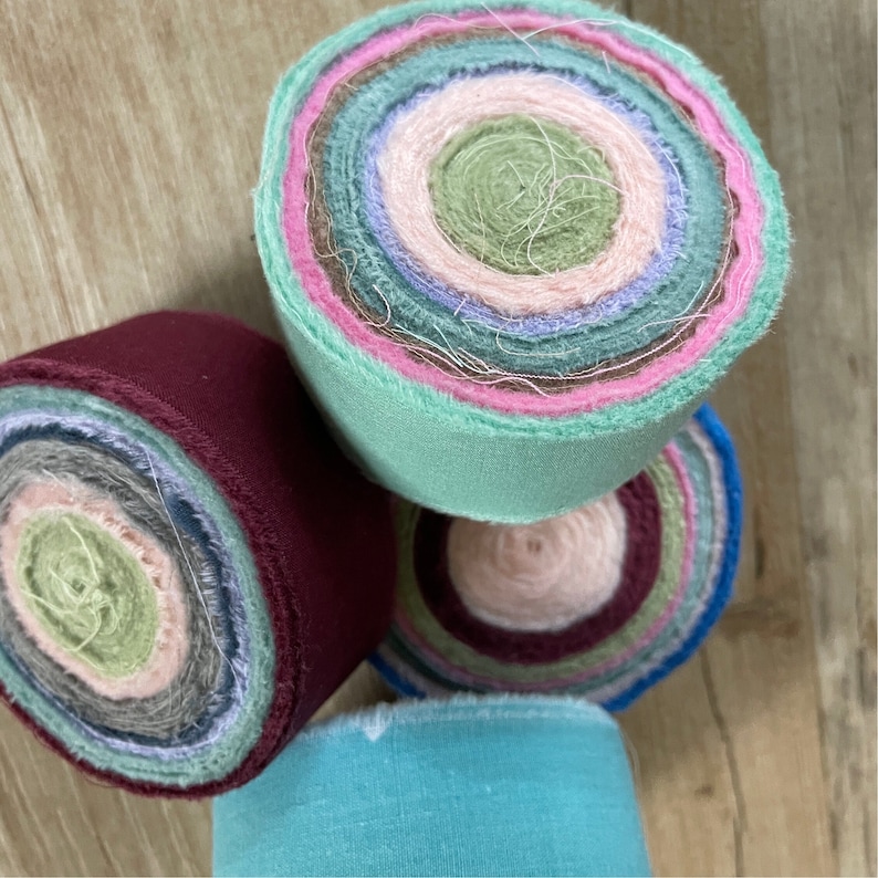 May include: Four rolls of fabric scraps in various colors, including teal, burgundy, pink, and green. The fabric is rolled into a circle and the layers are visible.