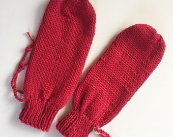 Könnte beinhalten: Ein Paar leuchtend rote Strickfäustlinge. Jeder Fäustling hat einen Kordelzug am Handgelenk und eine abgerundete Oberseite. Die Fäustlinge sind aus dickem, strukturiertem Garn gefertigt und liegen auf einer weißen Oberfläche.