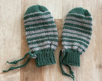 May include: A pair of green and gray striped knitted mittens with long ties. The mittens are made of a soft, warm yarn and have a simple, classic design.