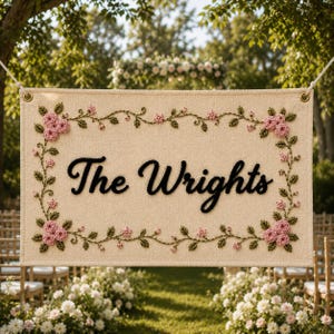Può includere: Striscione color crema con la scritta "The Wrights" in nero, circondato da un bordo floreale di rose rosa e foglie verdi. Lo striscione è sospeso da una corda bianca, ideale per un matrimonio.