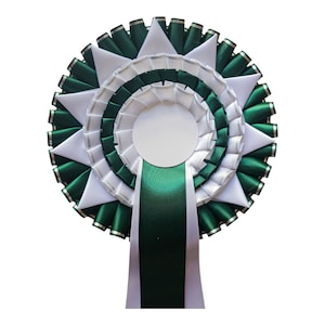 Könnte beinhalten: Eine dekorative Rosette in kreisförmigem Design mit abwechselnden Schichten aus weißem und dunkelgrünem Band. Die Rosette hat einen weißen Mittelkreis und ein langes, dunkelgrünes Band, das nach unten verläuft.