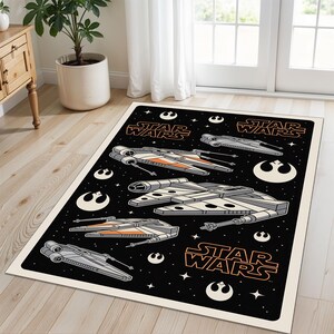 Puede incluir: Alfombra rectangular negra de Star Wars con naves espaciales blancas, grises y naranjas. Las palabras "STAR WARS" son naranjas. La alfombra tiene un borde crema y está sobre un suelo de madera.