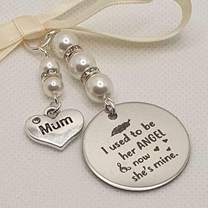 May include: A silver-toned metal charm ornament featuring a cream-colored satin ribbon bow. One charm is a heart engraved with "Mum" and the other is a round disc engraved with "I used to be her ANGEL & now she's mine." with white pearl beads.