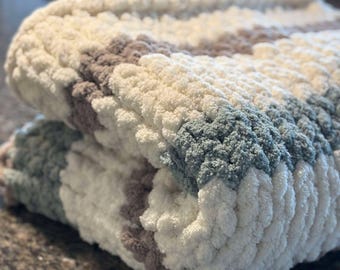 May include: A soft, chunky knit blanket with stripes of white, light brown, and light blue yarn.