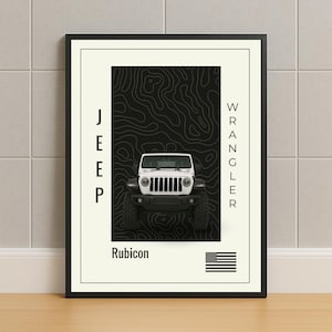 Puede incluir: Impresión enmarcada que presenta un Jeep Wrangler Rubicon blanco sobre un diseño de mapa topográfico negro. La palabra "JEEP" está alineada verticalmente a la izquierda y "WRANGLER" a la derecha. Una bandera estadounidense está en la esquina inferior derecha.