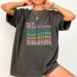 May include: A dark gray oversized t-shirt with the text "It's Wine o'Clock somewhere" printed in a rainbow of colors.