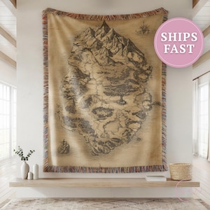 May include: A large, rectangular tapestry featuring a detailed, sepia-toned map of a mountainous island. The map is intricately drawn with forests, rivers, and a compass rose. The tapestry has a fringed border with red, brown, and blue threads. The text "SHIPS FAST" is in a pink circle.