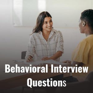 May include: Two people are seated at a table, talking and looking at each other. The text "Behavioral Interview Questions" is on the table in front of them.