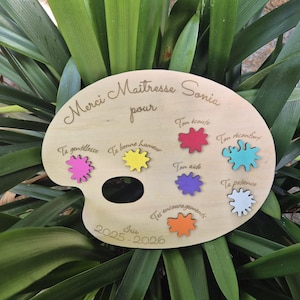 Peut inclure: Une plaque en bois clair en forme de palette d'artiste avec le texte gravé Merci Maîtresse Sonia pour, Iris, et 2025-2026. Elle comporte six taches de peinture colorées en rose, jaune, rouge, bleu, violet et orange avec des phrases gravées.